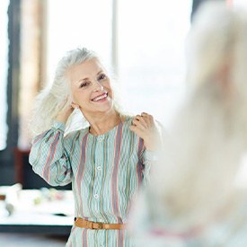 Woman with dental implants smiling in mirror while adjusting her hair