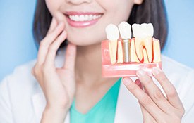 Dentist touching her cheek and holding up model dental implant